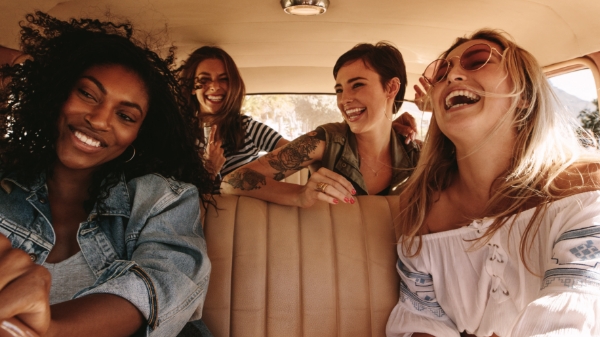 four women laugh and dancing inside a car