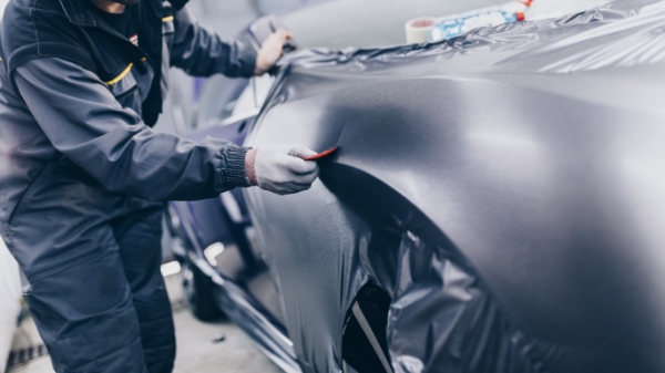 a man applies a silver vehicle wrap with an applicator tool