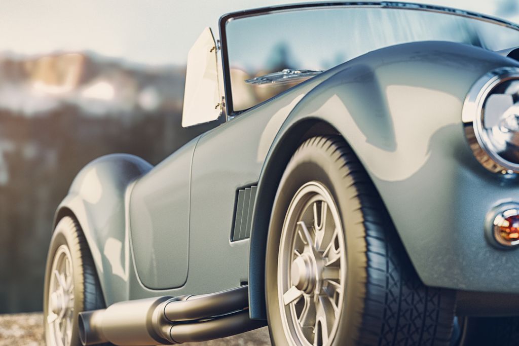 Close-up of a sleek, silver classic roadster with a flawless ceramic-coated finish, reflecting light off its curved body panels. The image captures the car's high-gloss surface and clean detailing, illustrating the long-lasting shine ceramic coating provides.