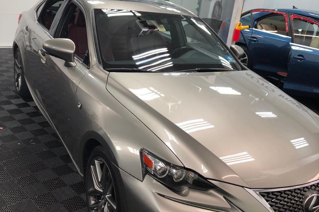 A silver Lexus sedan with a highly reflective, glossy finish sits inside a detailing shop, showcasing the results of a professional ceramic coating application.