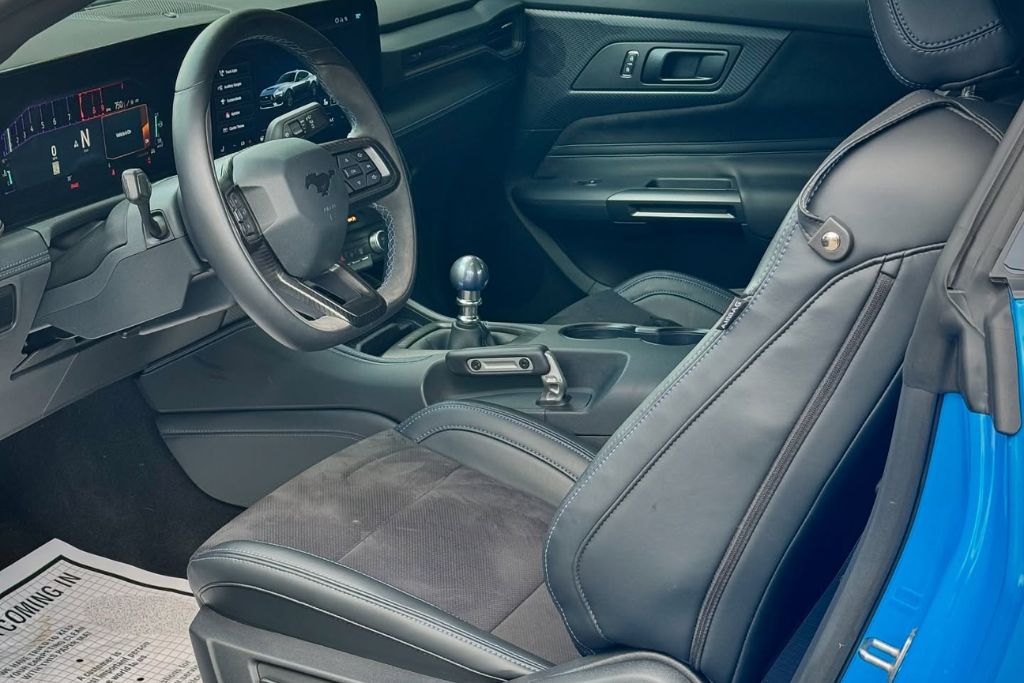 Close-up of a modern car’s black leather interior, showcasing the dashboard, seats, and gear shift in pristine condition, with sunlight subtly coming through the windows.
