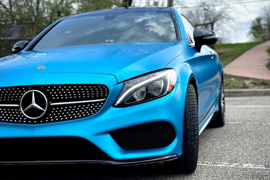 A vibrant blue Mercedes-Benz with tinted windows is parked in a lot, showcasing its glossy finish, bold grille, and sharp styling under natural daylight.