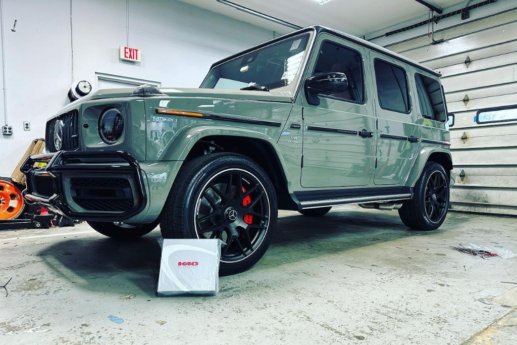 A sleek gray Mercedes-Benz G-Class SUV sits spotless inside a garage, with red brake calipers and a K40 radar system package placed by the front wheel. The vehicle's flawless paint and clean finish highlight the protective benefits of paint protection film.