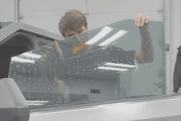 A technician applies a window tint film to a car door’s side window using a squeegee tool, smoothing out air bubbles during installation inside a bright, indoor garage.