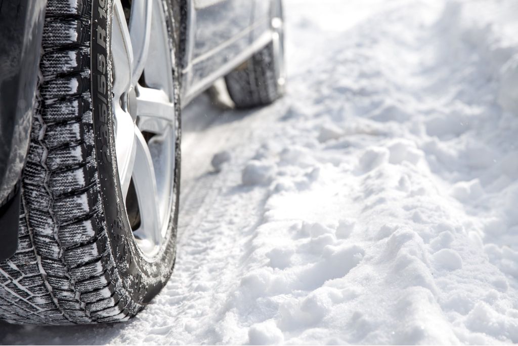 Close-up of a snow-covered winter tire driving on a snowy road, highlighting seasonal hazards that impact vehicle surfaces in New Jersey.