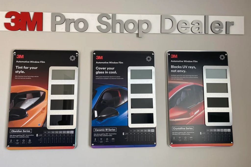 Display wall at a 3M Pro Shop Dealer showing side-by-side sample boards for 3M Obsidian Series, Ceramic IR Series, and Crystalline Series automotive window films, each highlighting different tint shades and performance benefits for heat rejection, UV protection, and style.