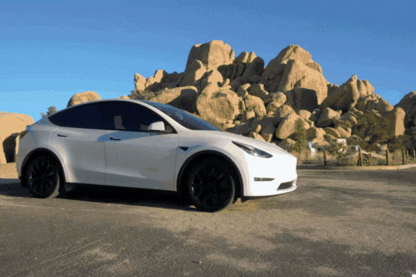 White Tesla Model Y with sleek black wheels parked in front of large desert rock formations, featuring tinted windows treated with 3M window film that reduces glare and heat for improved comfort and protection.