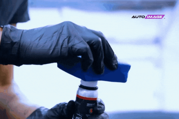 Close-up of a gloved hand prepping an applicator pad with ceramic coating solution inside a professional auto shop, showcasing proper application technique used at Auto Image locations in Brick and East Brunswick, NJ.