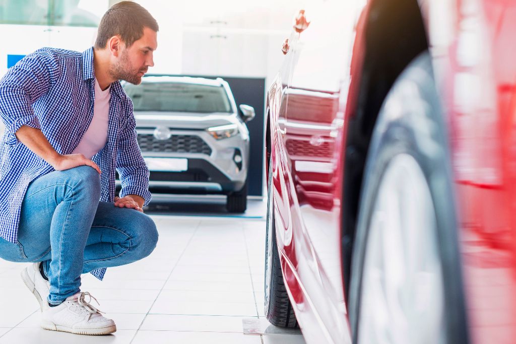 Man inspecting the paint finish on a red car in a well-lit showroom, reflecting the importance of timing and surface readiness when deciding how long to wait before applying ceramic coating.