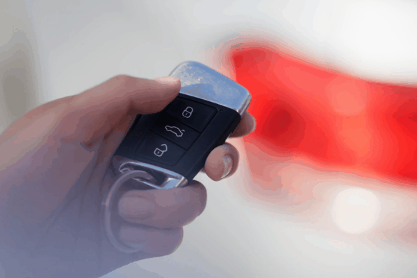 A close-up of a hand holding a car remote key fob with lock, unlock, and trunk buttons visible.