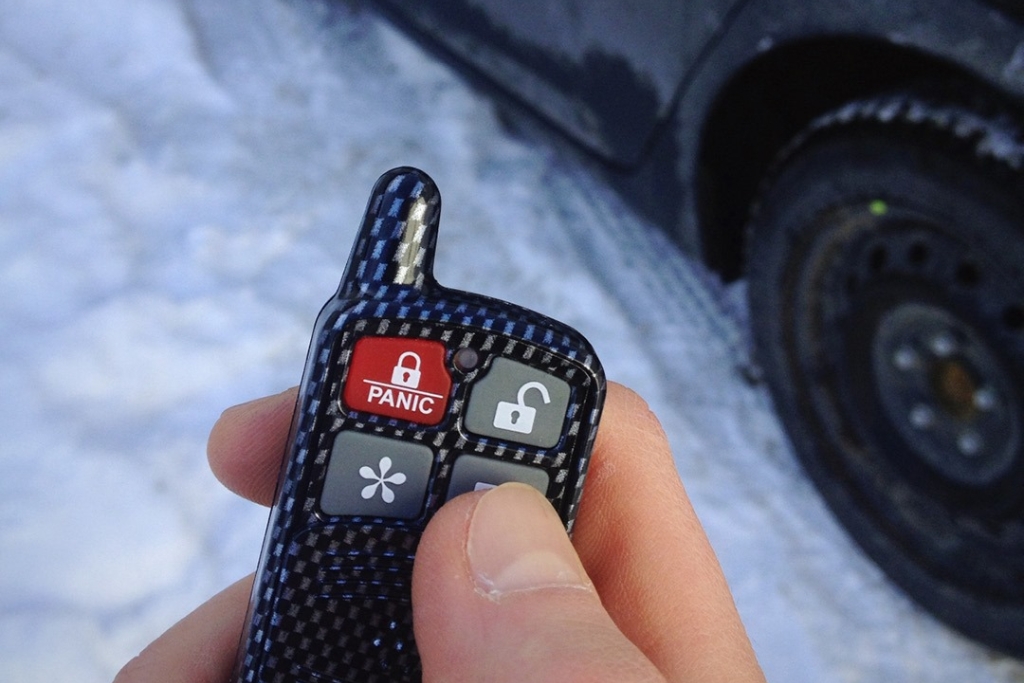 Close-up of a person holding a carbon fiber-style remote start fob in front of a snow-covered car in New Jersey illustrating how Auto Image installations help boost resale value and vehicle appeal through added winter convenience