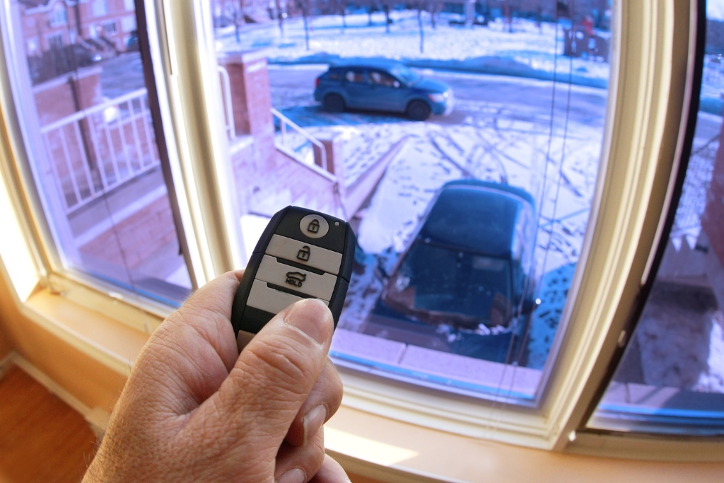 Person using a remote car starter from inside their home to start a snow-covered vehicle parked outside showcasing the benefits of a remote car starter from Auto Image in New Jersey for cold morning comfort and visibility