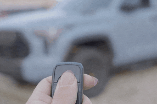 Person pressing a remote start key fob to warm up a light blue truck in cold weather showing the benefits of a remote start system installed by Auto Image in New Jersey