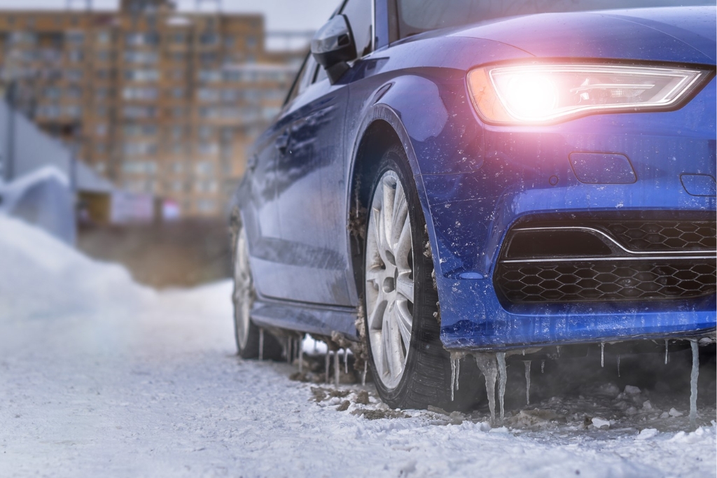 Blue car warming up with headlights on and icicles hanging from the bumper on a snowy New Jersey street highlighting enhanced safety and legal considerations with a remote start system installed by Auto Image
