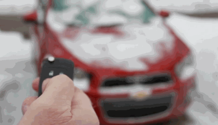 Person pointing a remote start key fob at a red Chevrolet car covered in snow.
