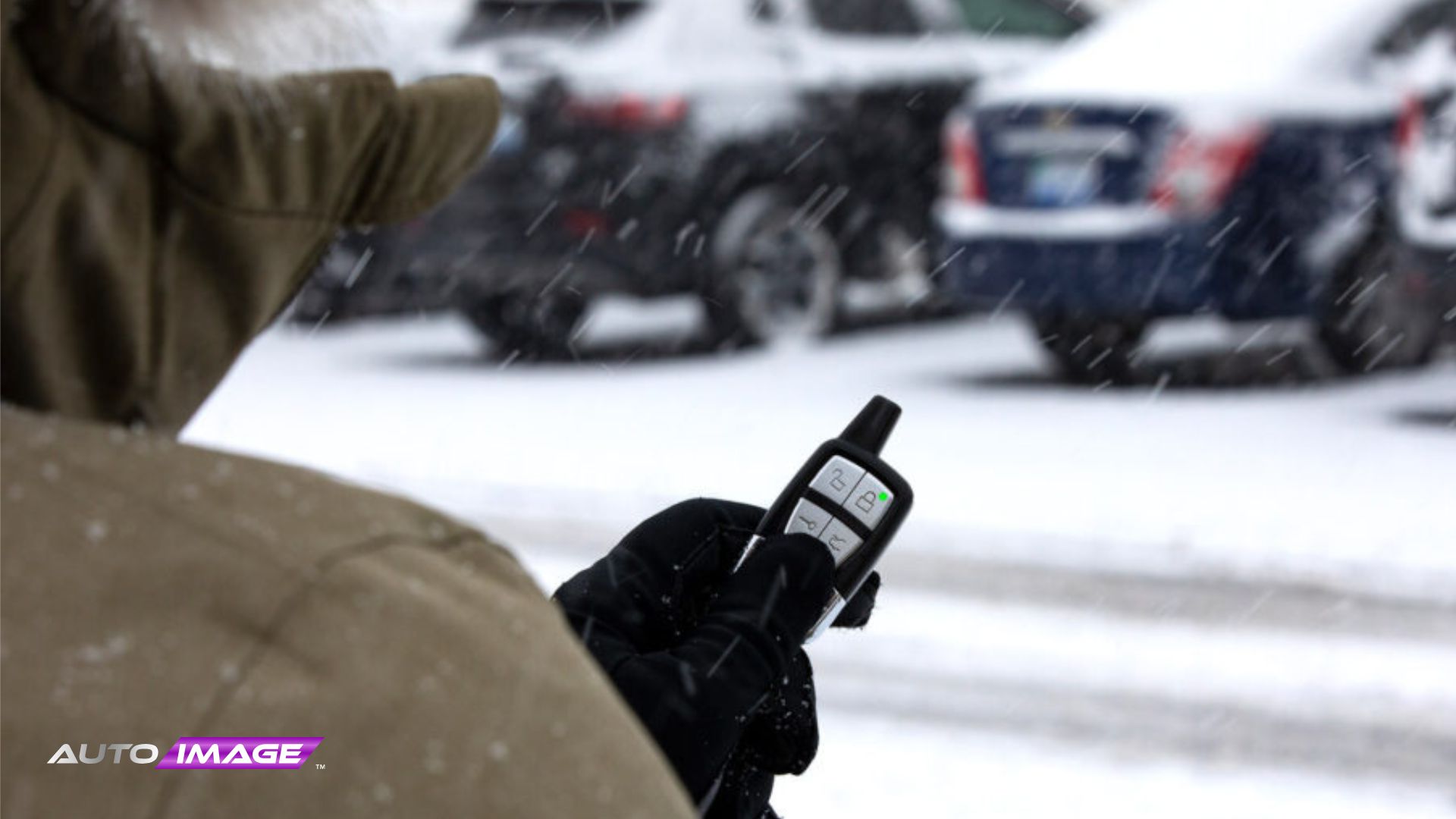 Person in a winter coat using a remote start remote in a snowy parking lot.