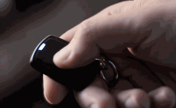 Close-up of a hand pressing a button on a small black remote start key fob, with a soft blue light indicator.