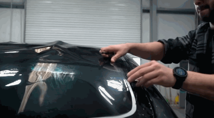 Installer stretches and aligns Window Film across the curved rear glass of a Tesla before final placement. Reflections on the glossy surface show the film being positioned for a perfect custom fit.