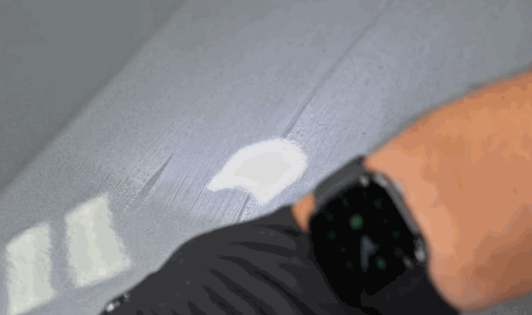 Close up of a hand wearing a black glove polishing a car panel where a small white spot of ceramic coating sits on the paint surface. The glossy panel reflects light as the coating is spread and leveled during the detailing process.