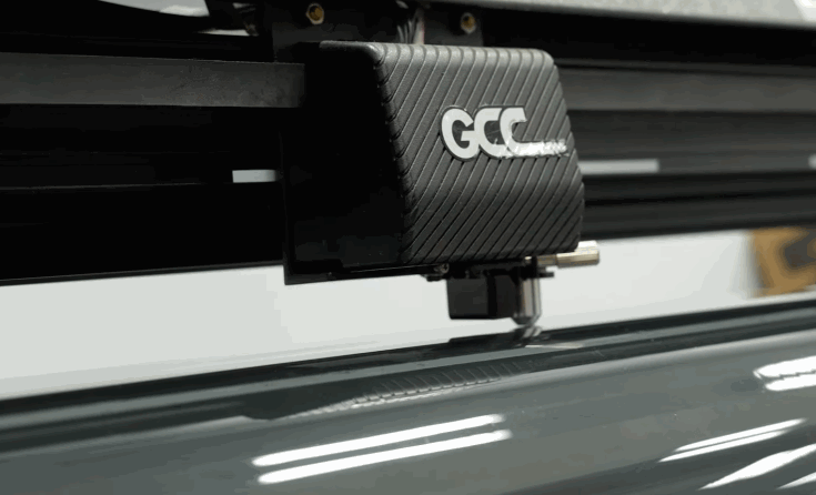 A GCC cutting machine trims window tint film for a precise replacement fit. The close up shows the cutter working along a sheet of tint.