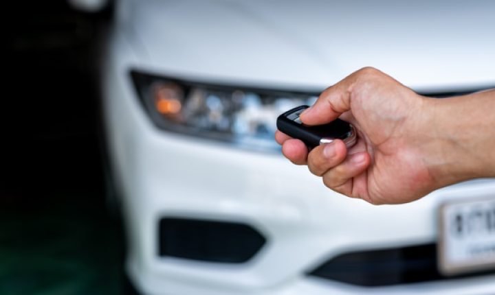 Hand of a man holding and push remote control of white car